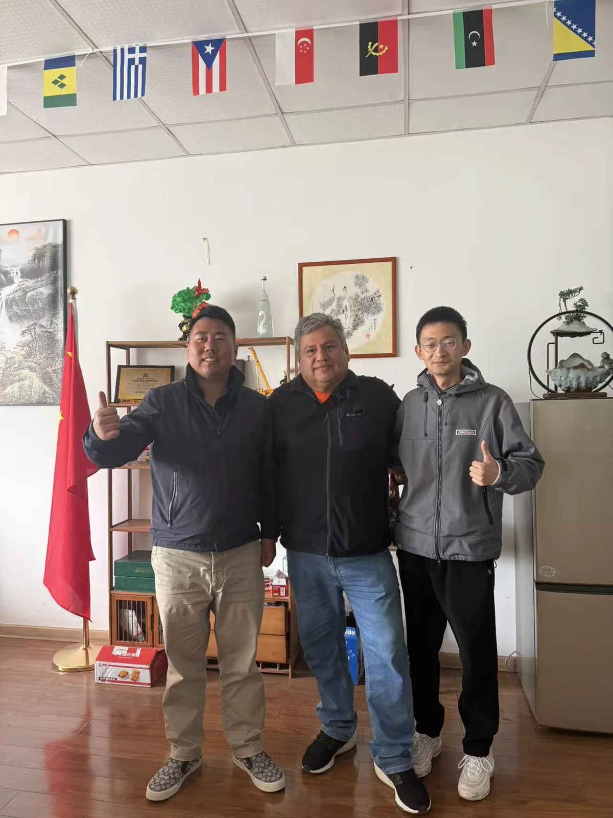 Three people posing in front of the YUYAN-brand wall in the office
