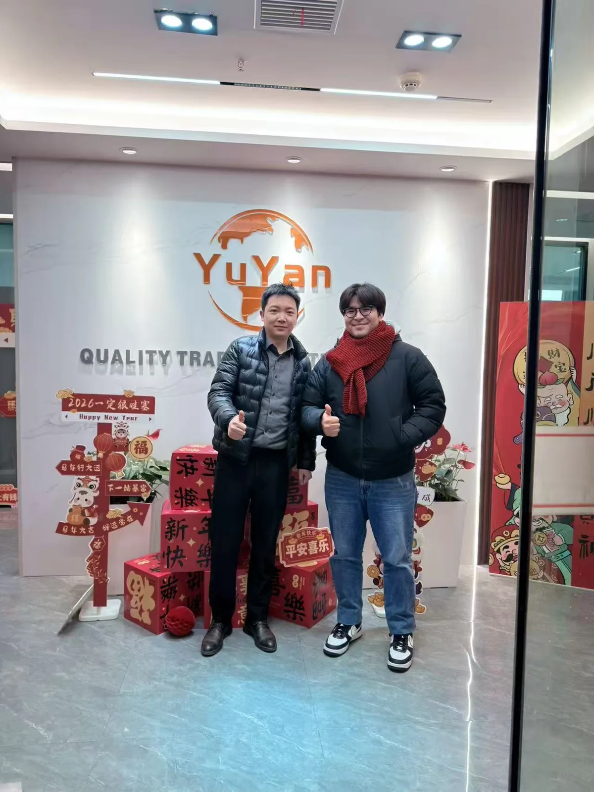 Two people posing in front of the YUYAN-brand wall in the office