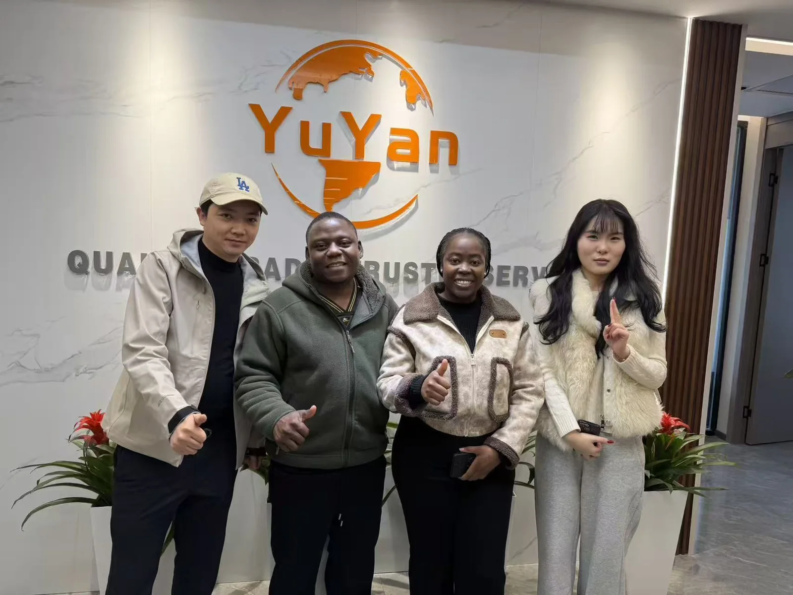 Four people posing in front of the YUYAN-brand wall in the office